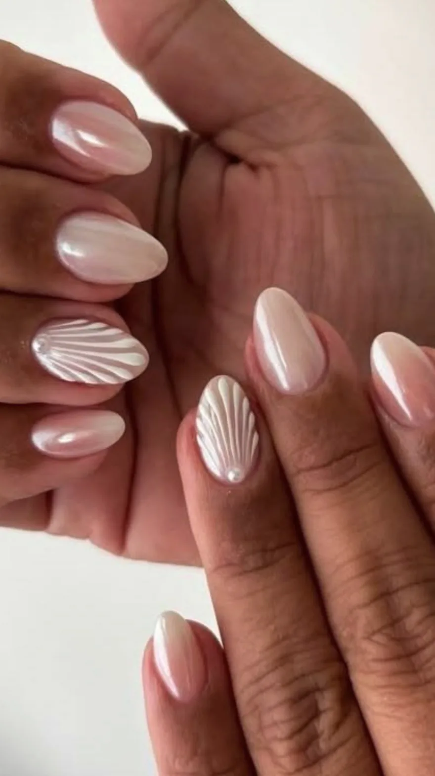 Nude pink almond nails featuring detailed white 3D shell textures and small pearl embellishments.