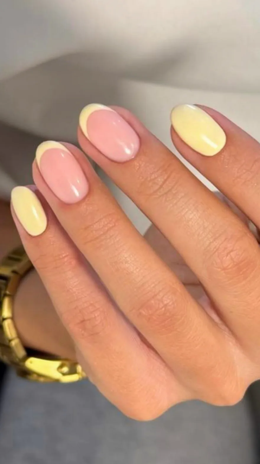Hand showing short almond nails alternating between a soft pink base with yellow tips and solid butter yellow polish.