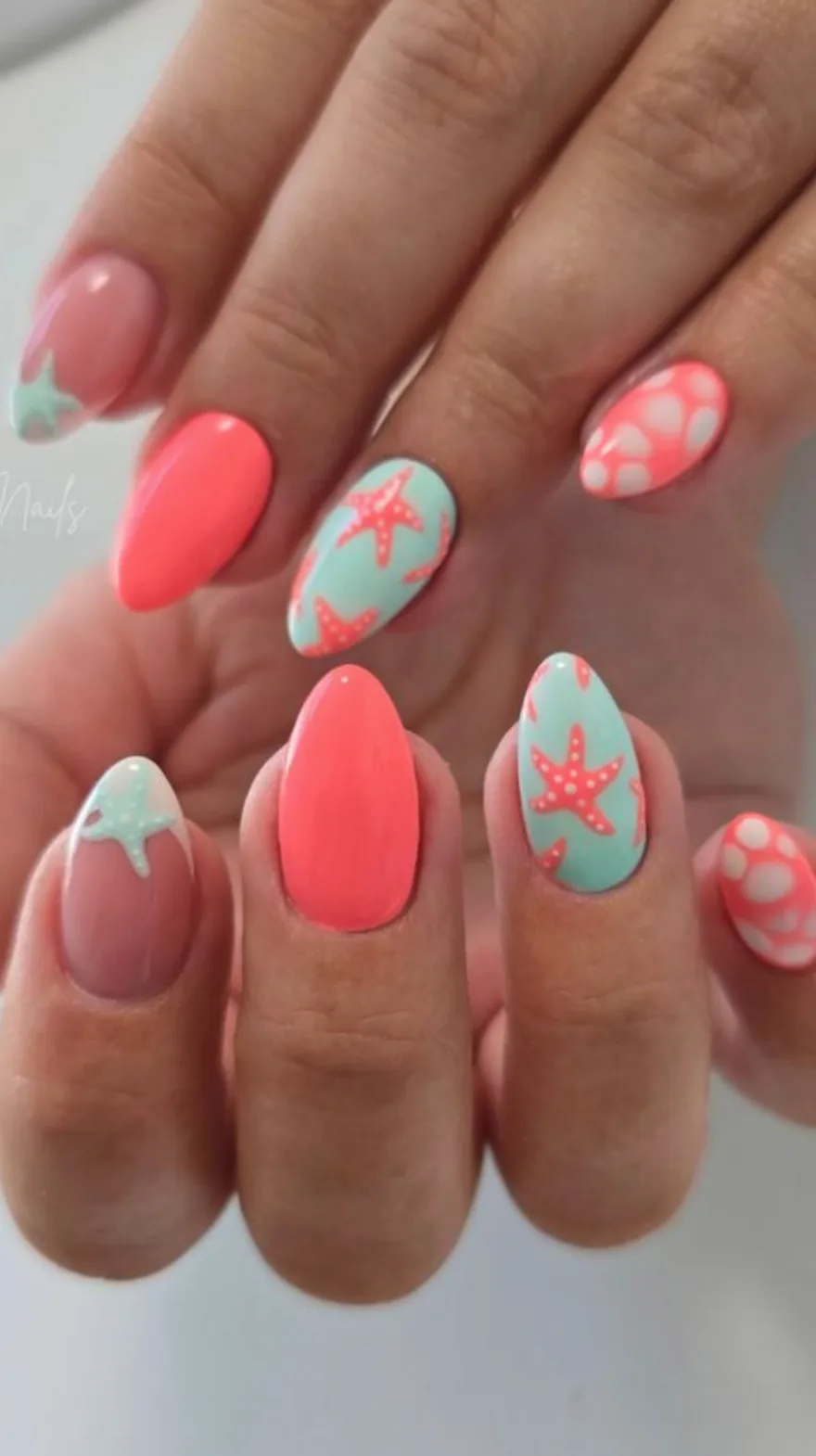 Pointed almond nails featuring a mix of bright coral and mint green bases with white polka dots, french tips, and starfish designs.