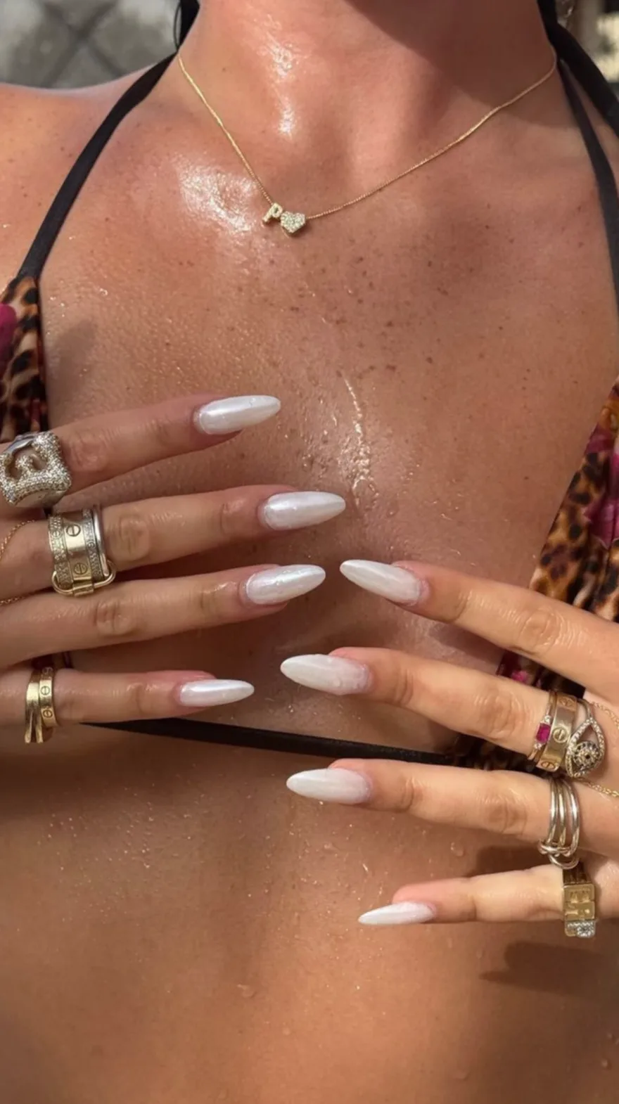 Long almond nails with iridescent pearlescent white polish paired with stacked gold rings and a leopard print bikini.