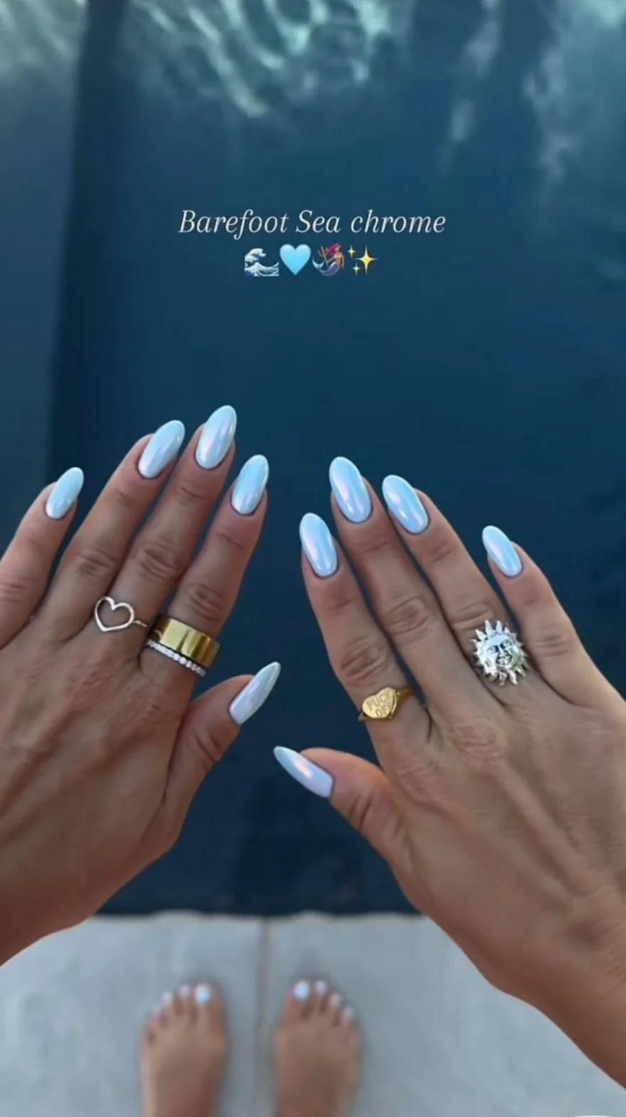 Pointed almond nails with a blue-shifted chrome pearl finish held over a dark blue swimming pool.