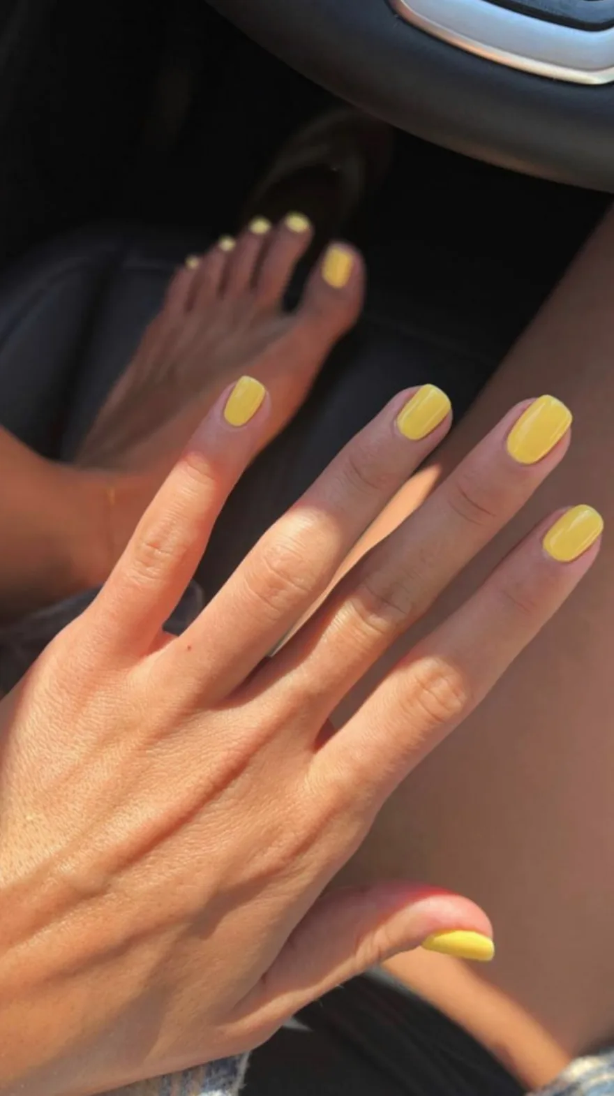 Bright yellow manicure and matching pedicure on hands and feet showing a vibrant glossy finish.